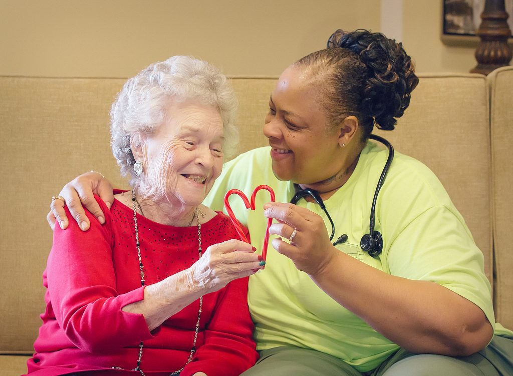 A nurse and a memory care patient smile at each other holding a heart